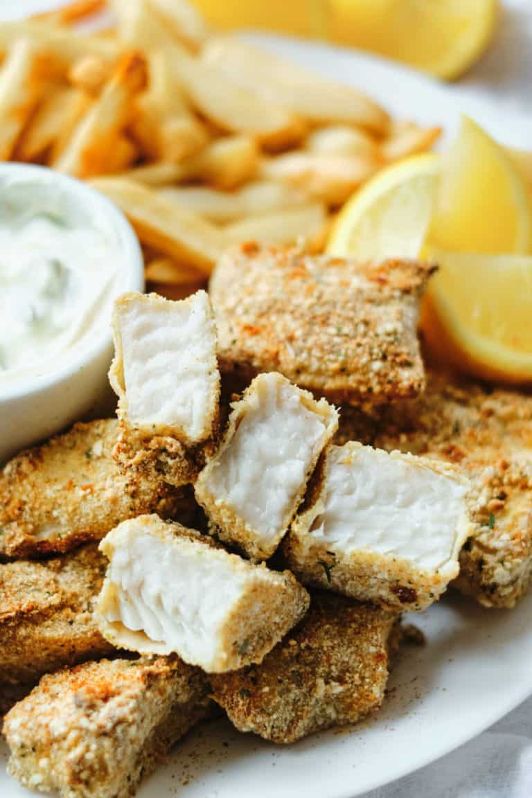 close up view of a serving of fish sticks on a white plate with lemon wedges and tartar sauce