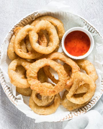 the finished air fryer frozen onion rings served on a ceramic plate with a small bowl of dipping sauce