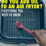 A HAND ADDING OIL TO AN AIR FRYER BASKET WITH A BRUSH