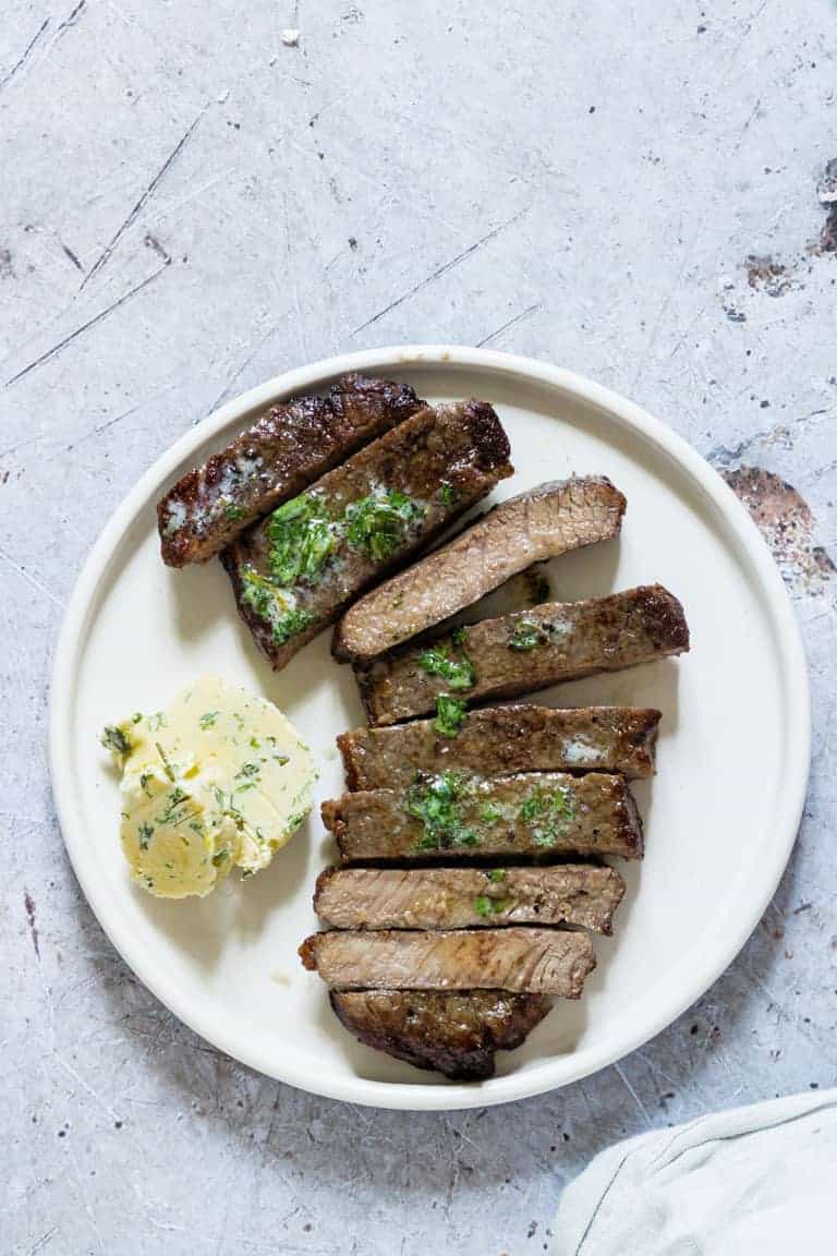 close of up of air fryer steak sliced on a plate with herb butter