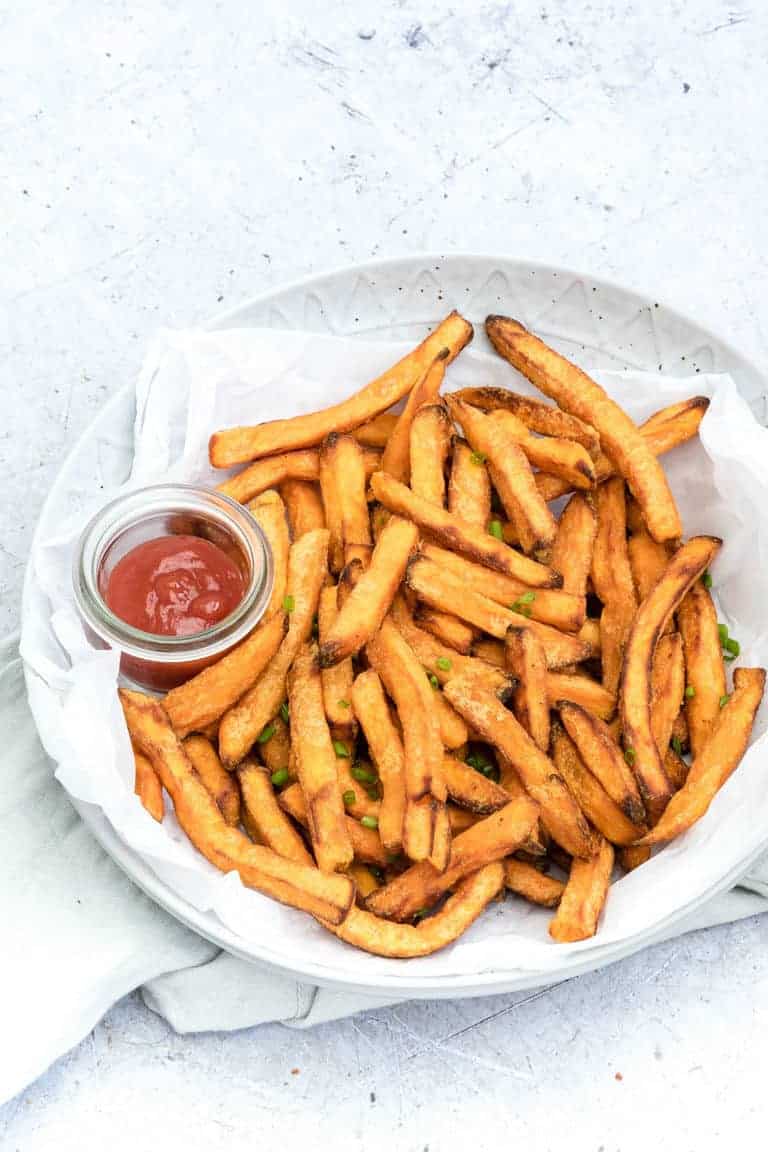 Air Fryer Sweet Potato Fries on a white plate with a side of ketchup placed on a white cloth napkin