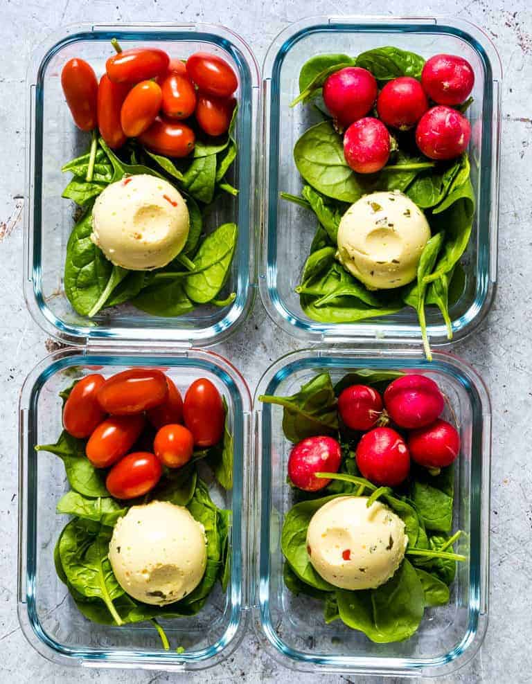 top-down view of four glass containers containing salad greens, tomatoes and Instant Pot Egg Bites