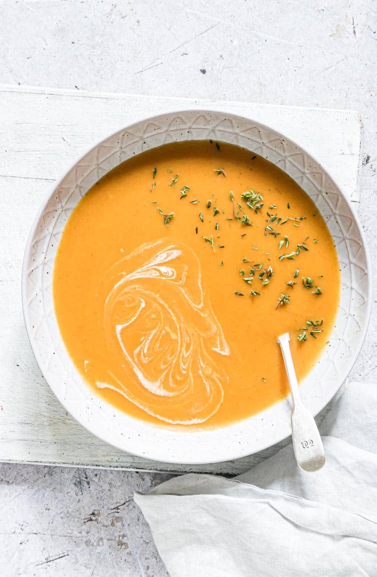 a bowl of jamaican pumpkin soup topped with coconut milk and pumpkin seeds
