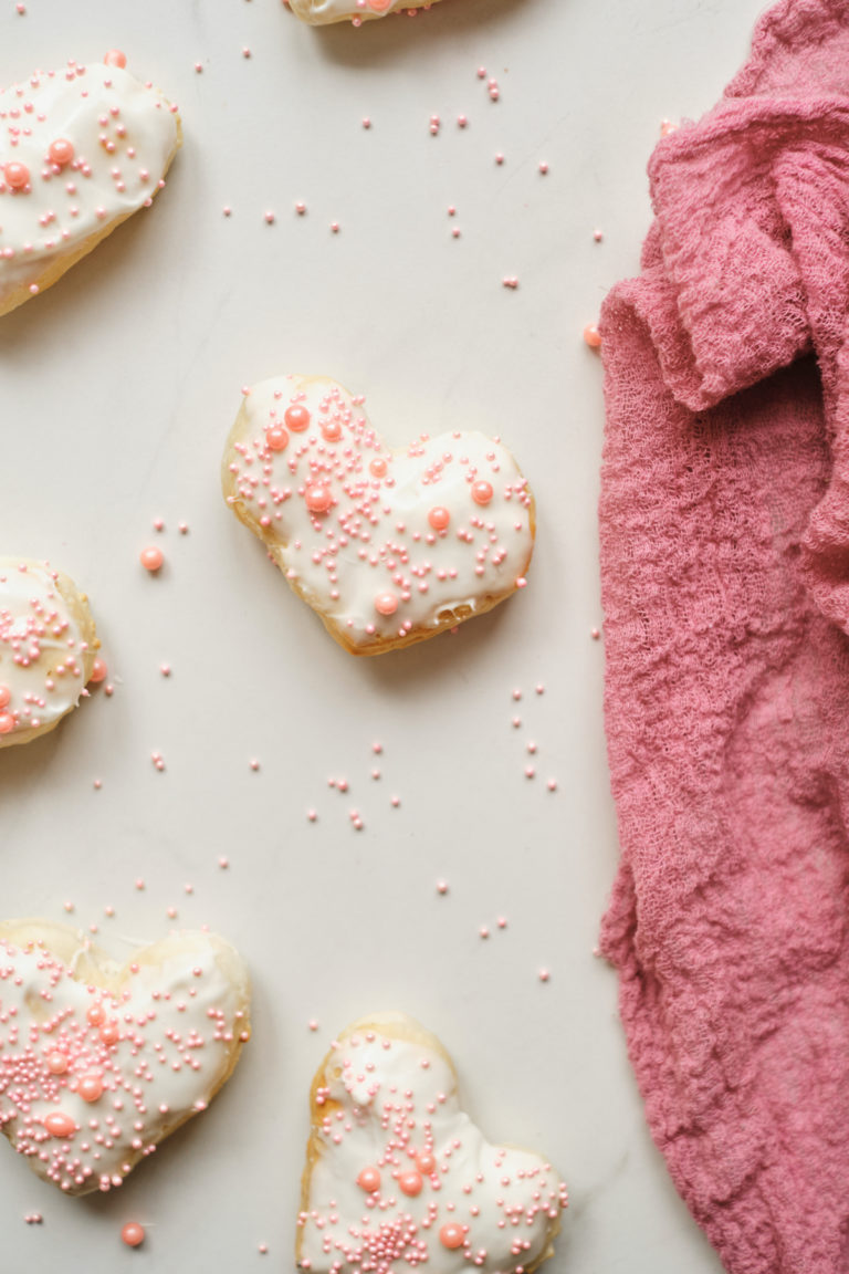 decorated valentines donuts on a countertop next to a pink kitchen towel