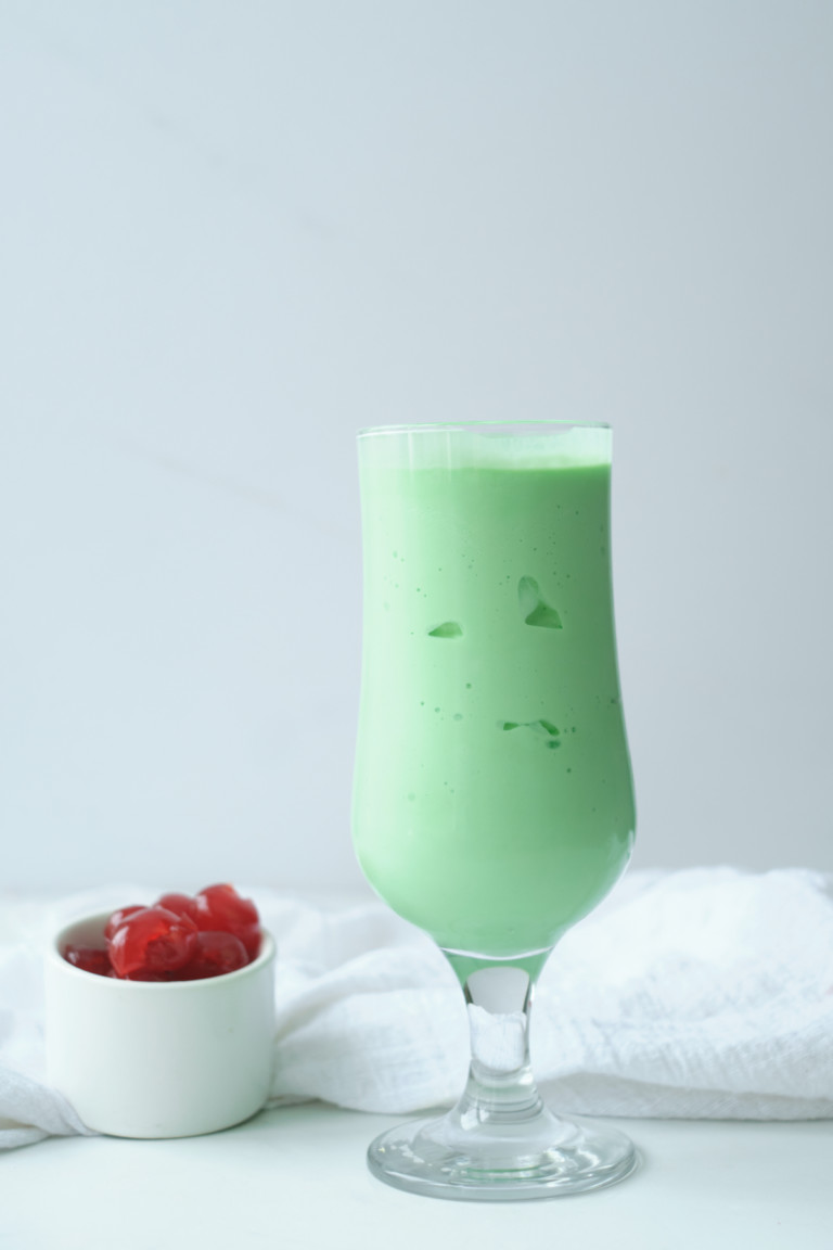 one shamrock shake in a glass with a bowl of cherries beside it