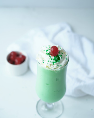 one shamrock shake served in a glass and topped with whipped cream, sprinkles and a cherry