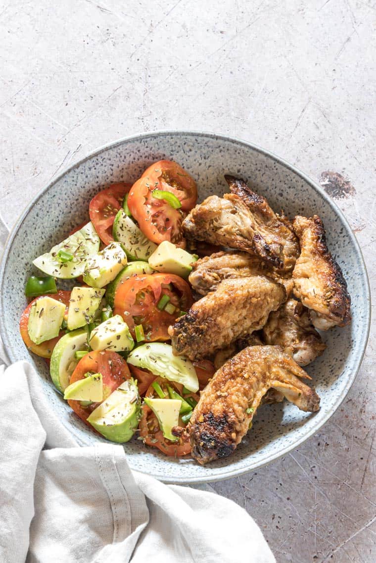 Smoked chicken wings in a white and grey spotted bowl with a side of salad.