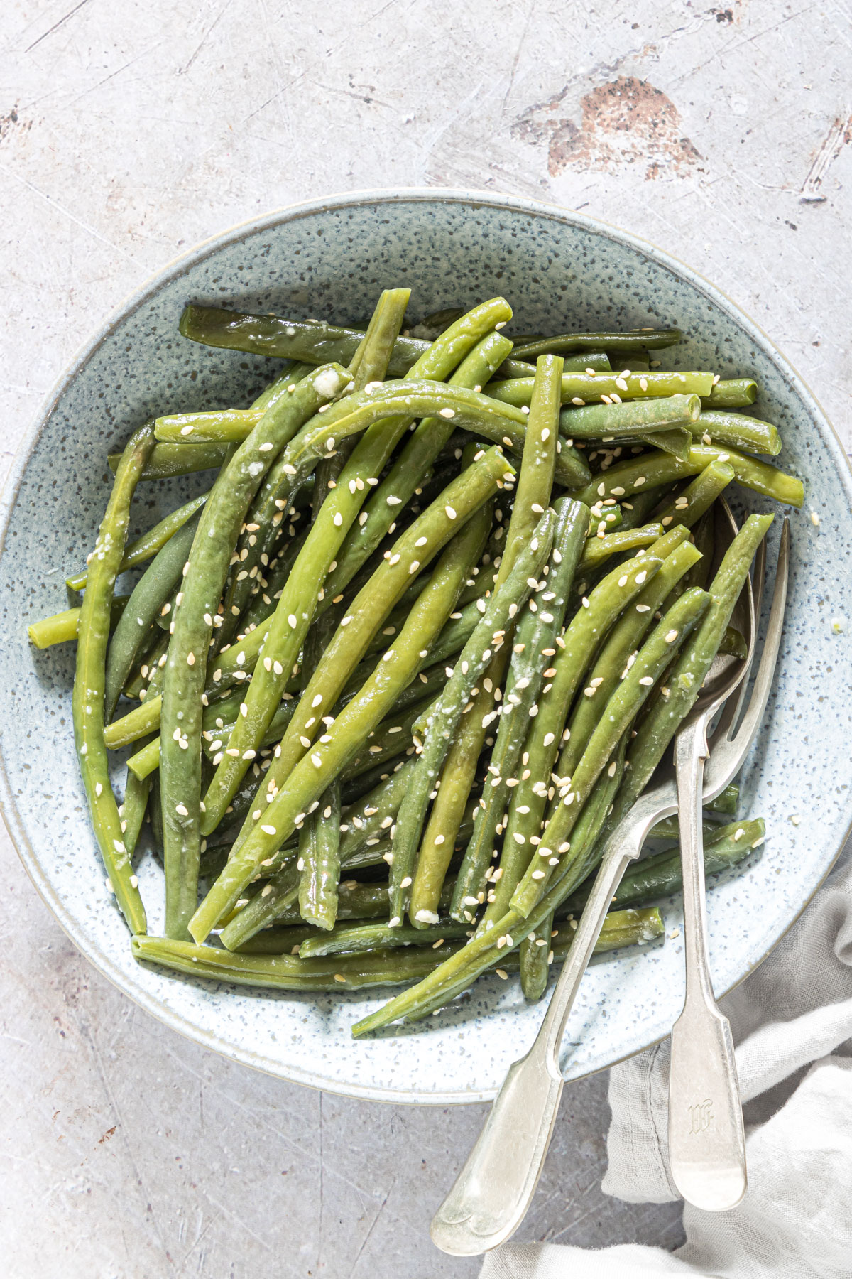 the finished sesame instant pot green beans served in a ceramic bowl with silverware and a cloth napkin