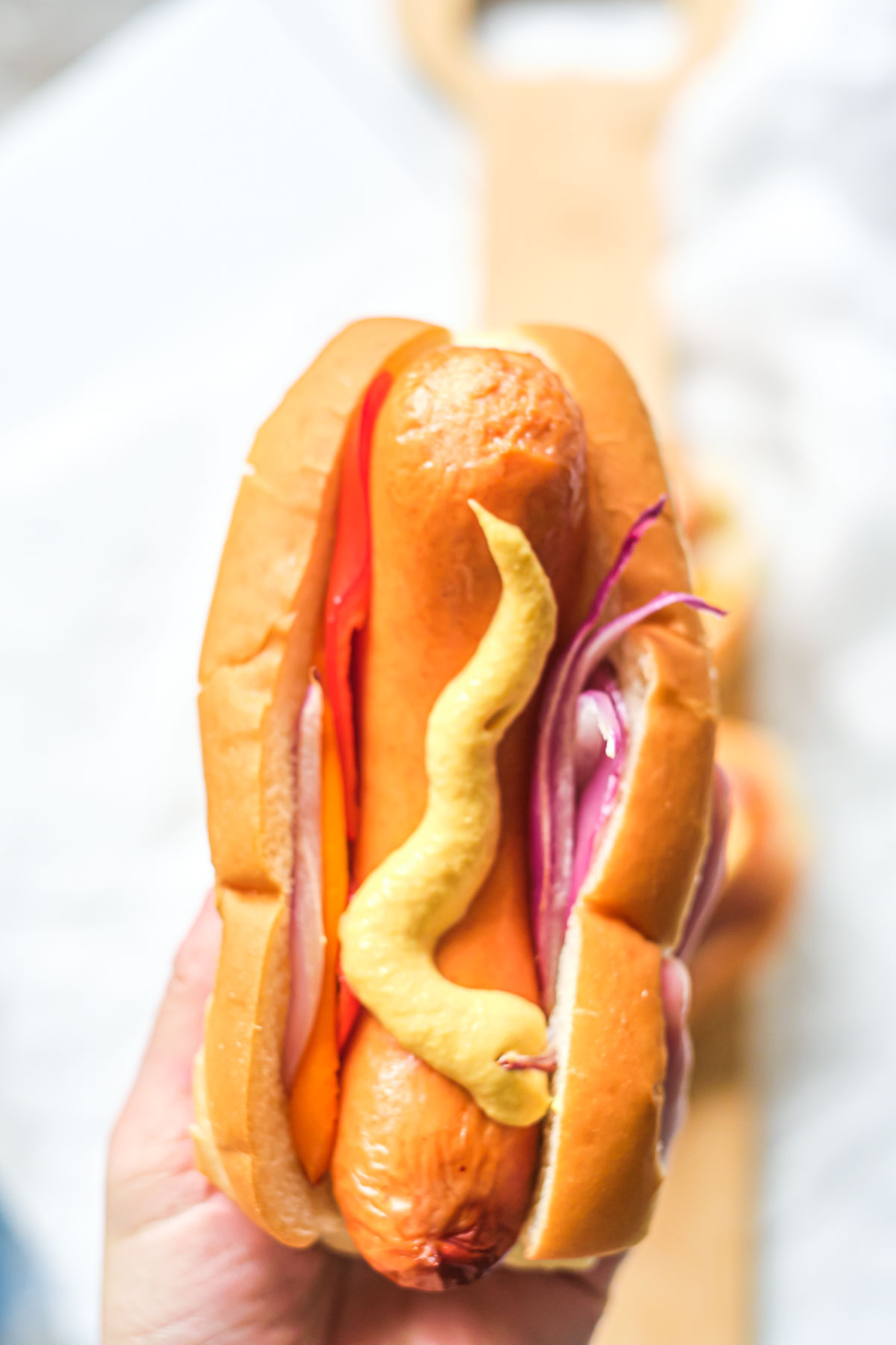 a hand holding air fryer brats in a bun with mustard