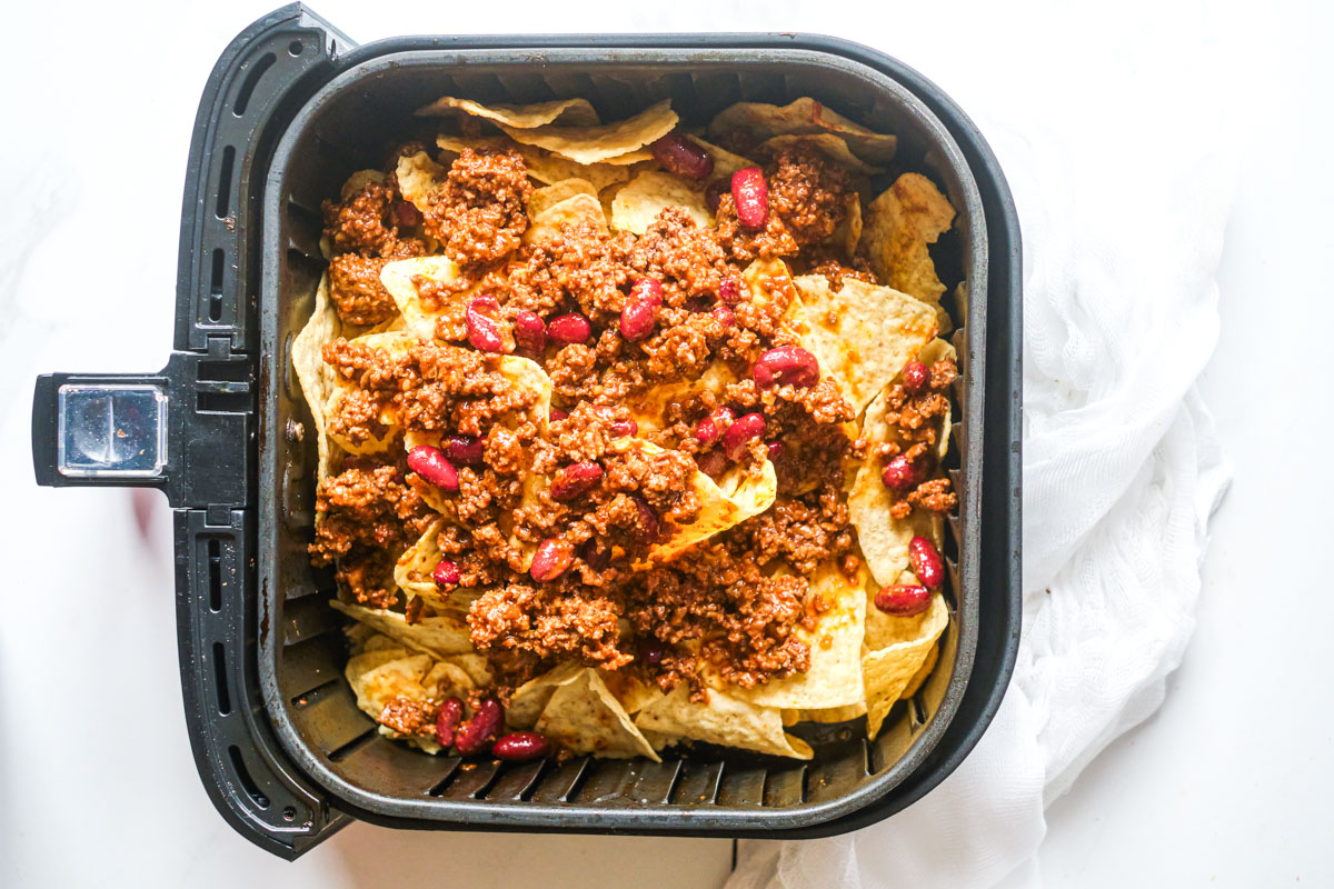 close up with cheese, ground beef chili and tortilla chips  in an air fryer basket