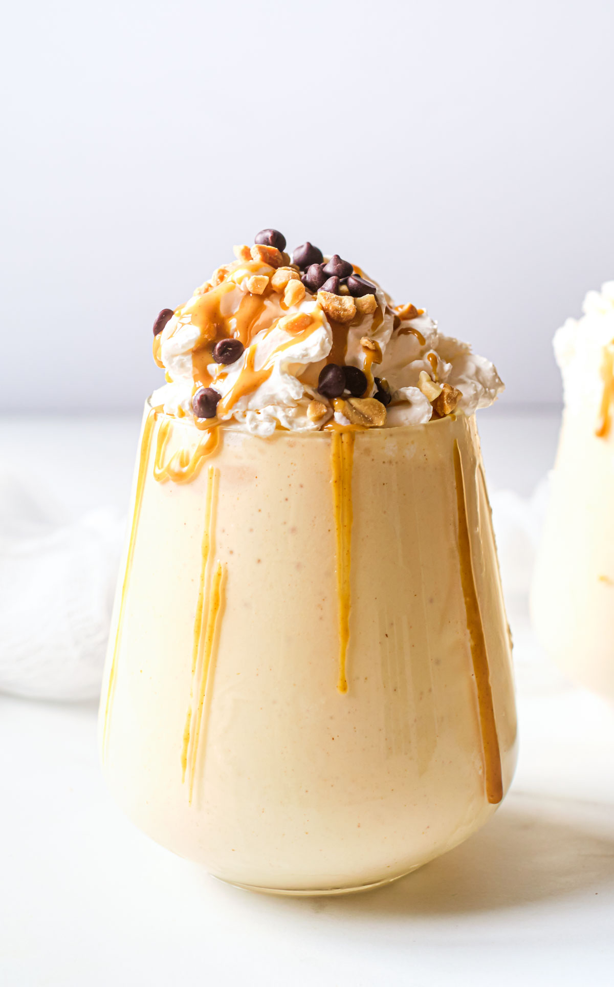 One indulgent peanut butter and cookie milkshake on a table with cream, chocolate chips, peanuts and caramel sauce
