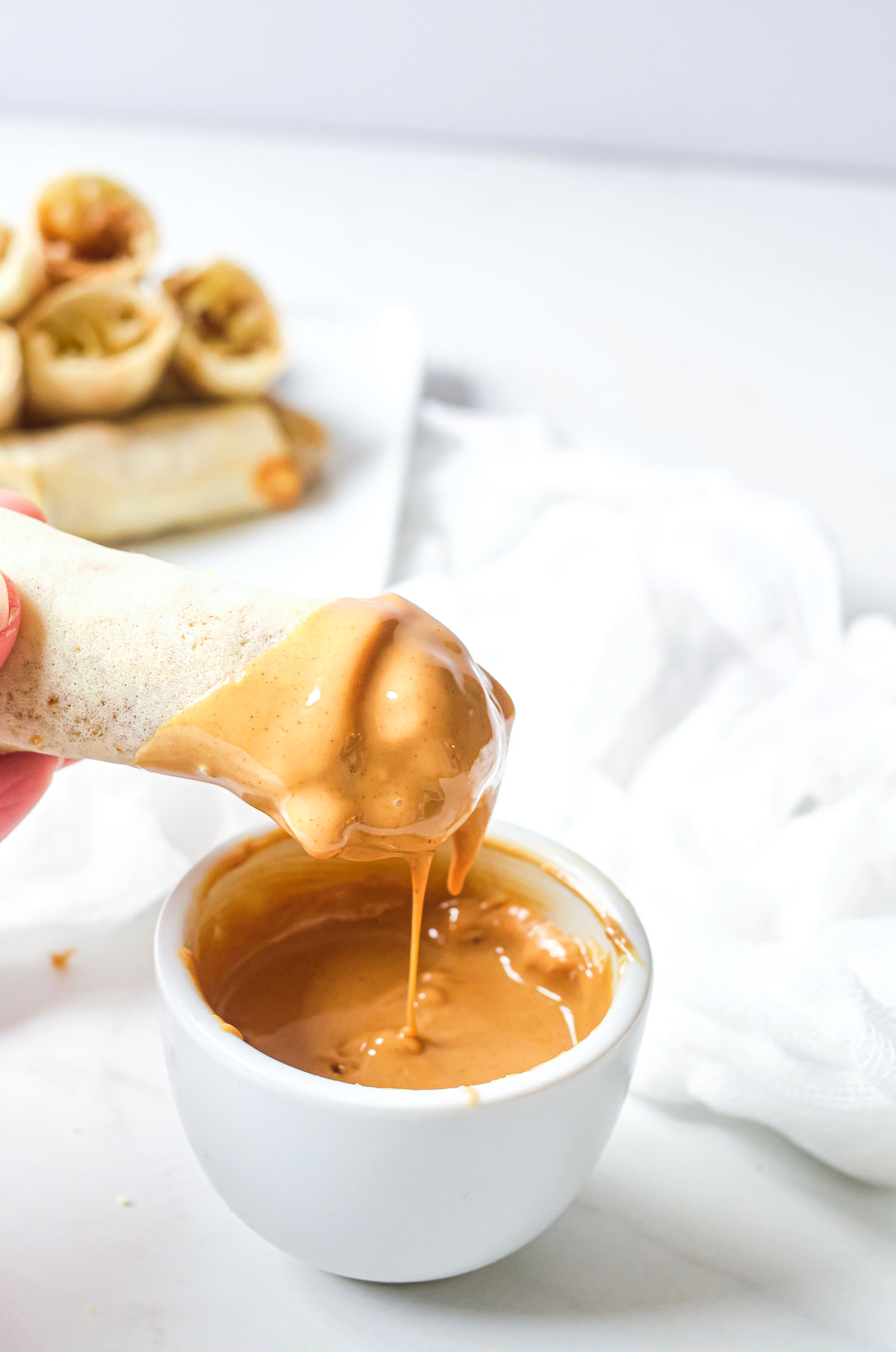 peanut butter banana spring roll being dipped in peanut butter sauce
