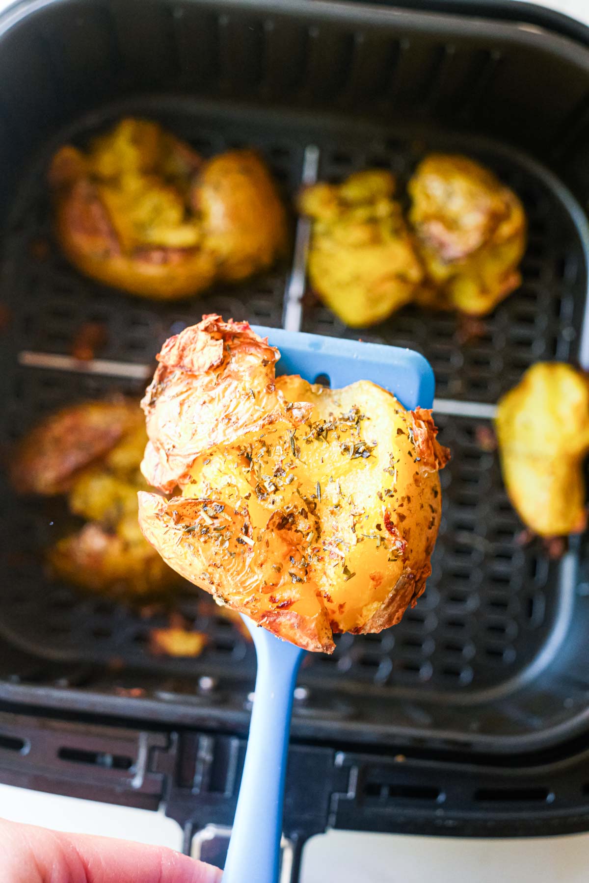 a spoon holding an air fryer smashed potato with herbs over an air fryer