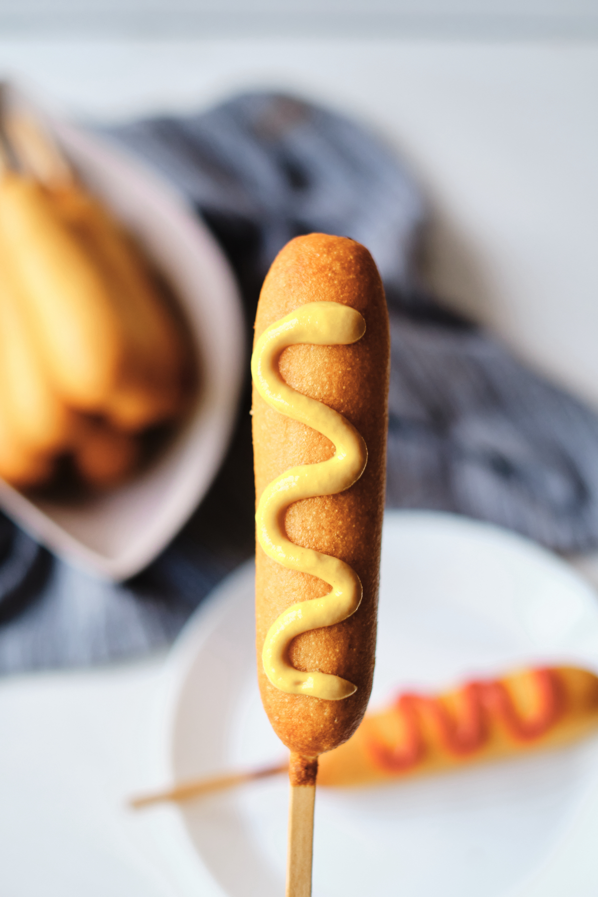 a cooked corn dog held upright with  mustard on it