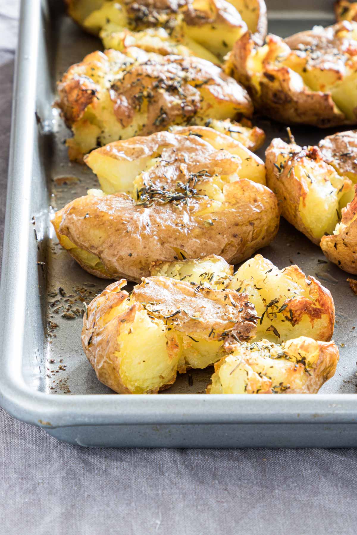 close up of crispy smashed potatoes  with herbs on a baking tray