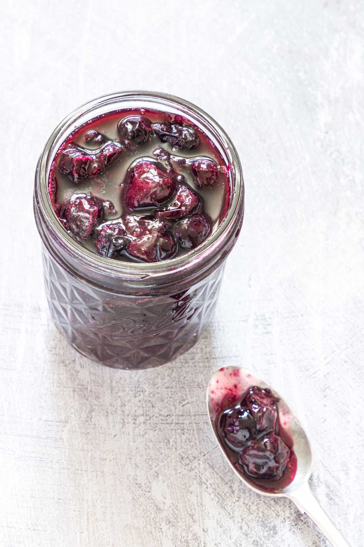 a jar full of homemade blueberry compote with a teaspoon next to it