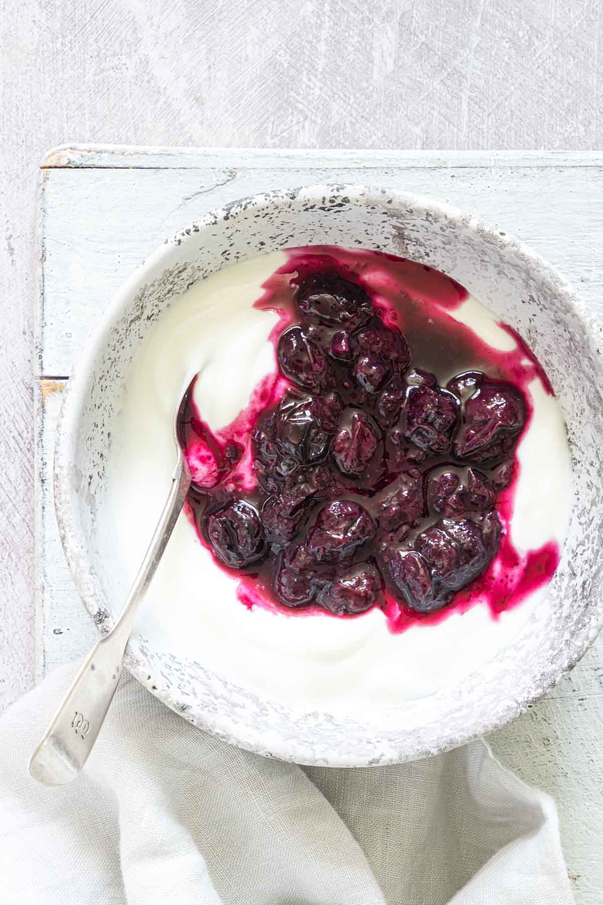 A bowl with blueberry sauce over some yogurt with a spoon tucked in on the side