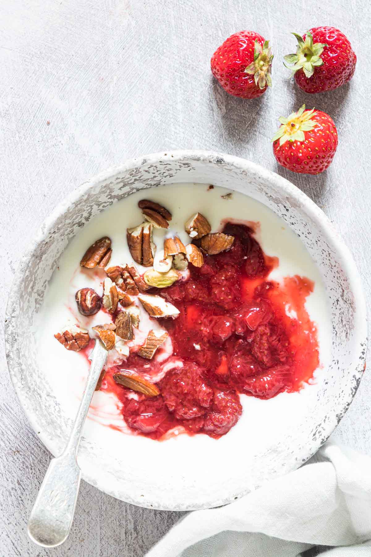 a bowl of greek yogurt topped with strawberry compote with nuts and a spoon