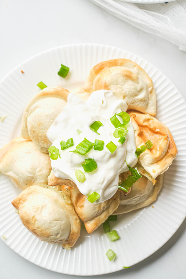 close up view of a plate of cooked air fryer frozen pierogies topped with sour cream and green onions