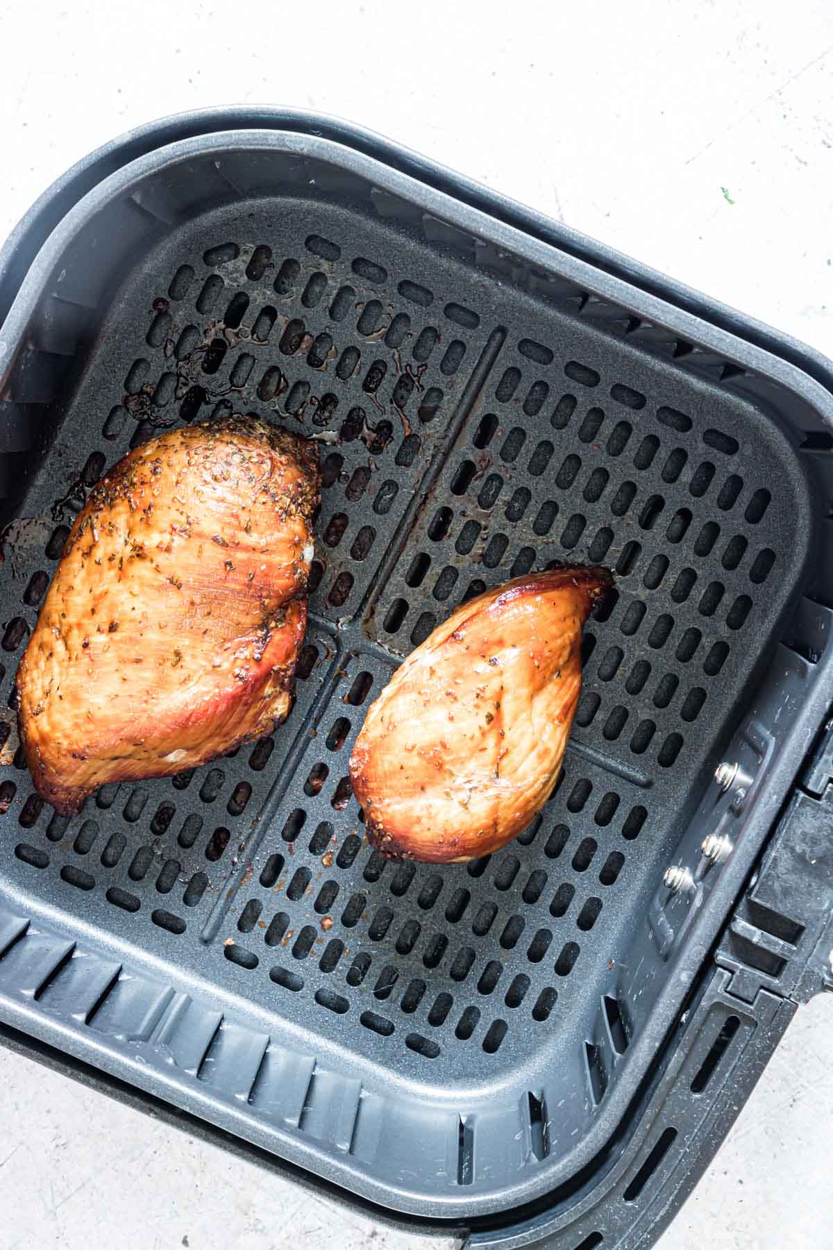 top down view of two cooked frozen chicken breast inside the air fryer basket