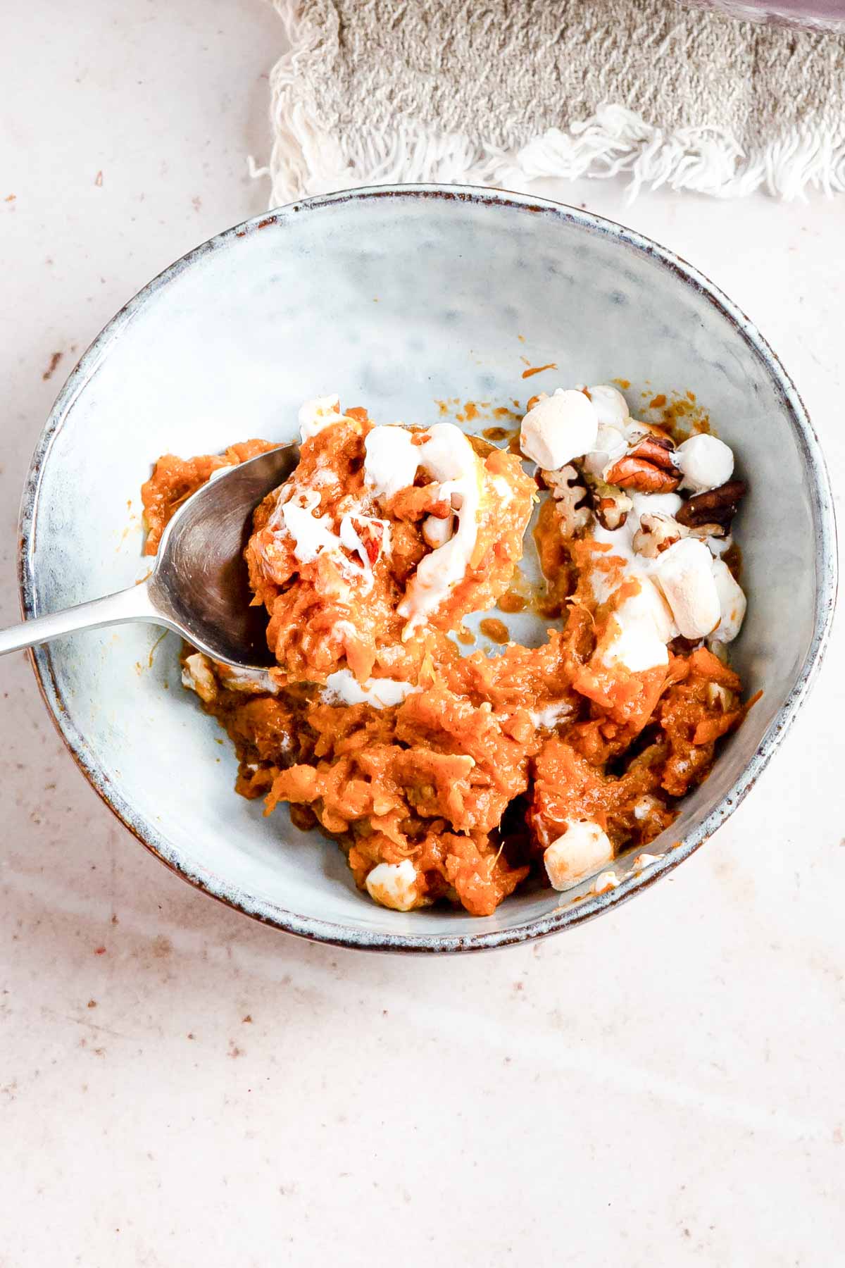 one portion of sweet potato casserole in a ceramic bowl with spoon removing a bite