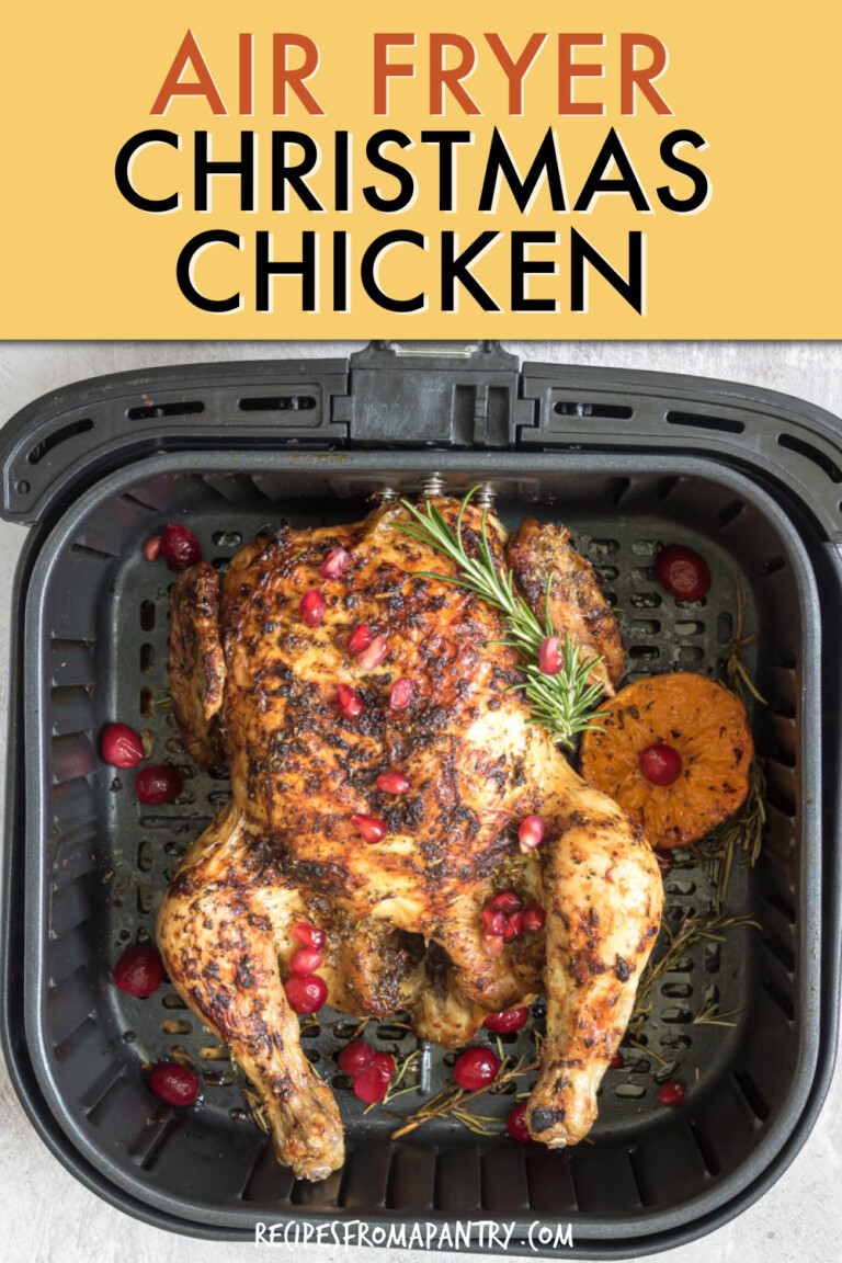 a whole roast chicken in an air fryer basket garnished with orange slices and cranberries