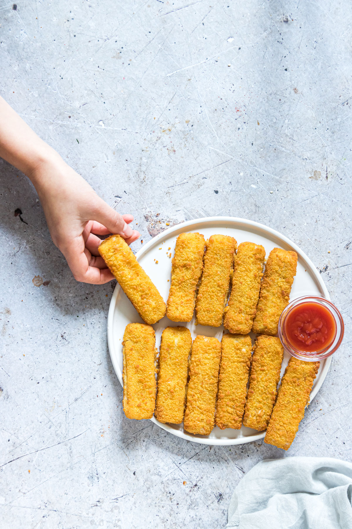 kids hand taking one of the air fryer frozen fish sticks from a white plate