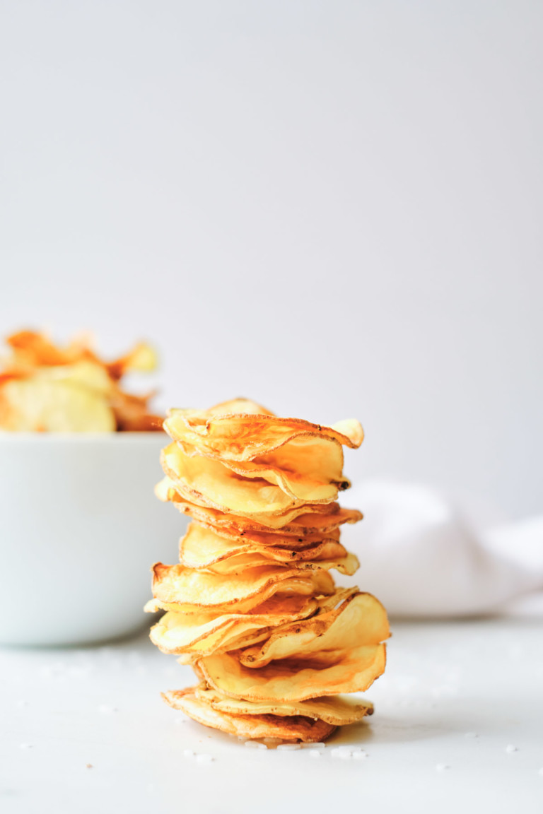 the completed air fryer potato chips stacked in front of a white bowl