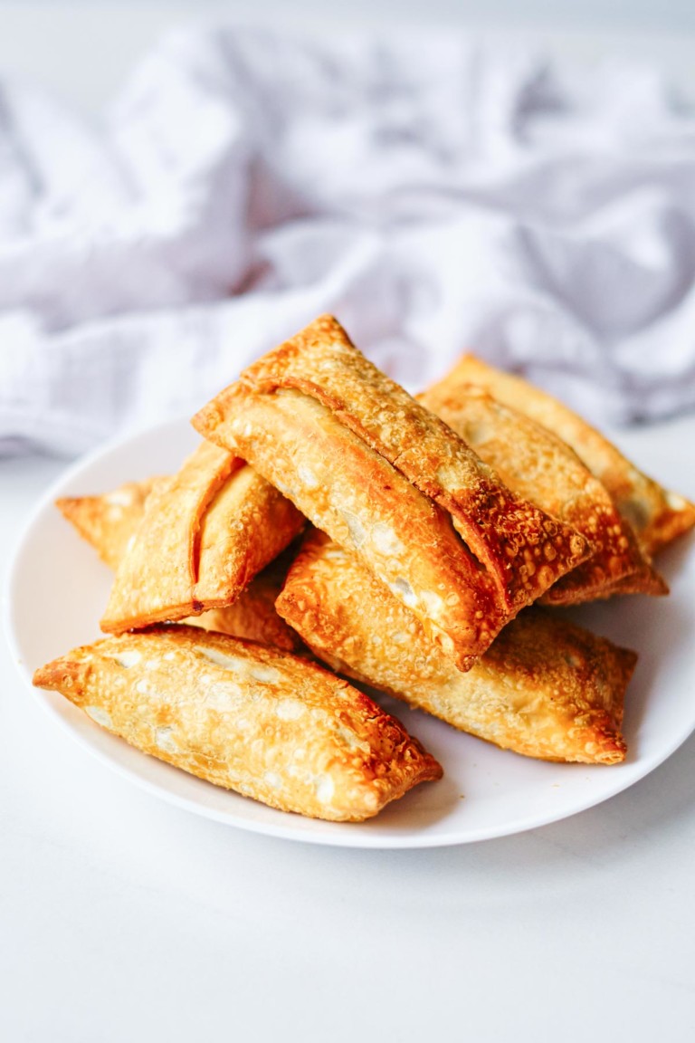 frozen egg rolls piled on a white plate and ready to be cooked in air fryer