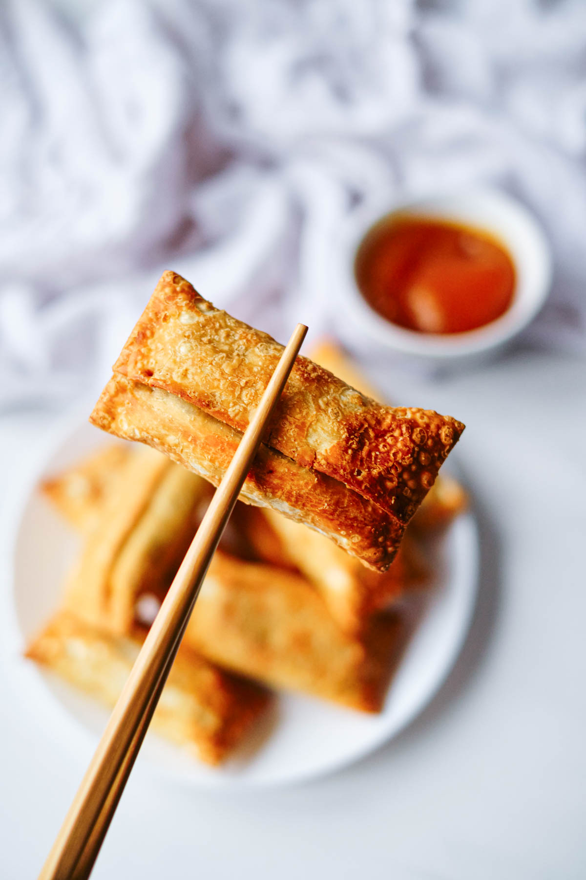 one finished frozen egg rolls in air fryer being held with chopsticks