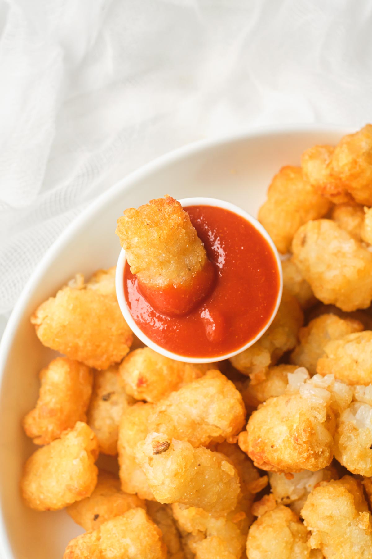 close up view of the frozen tater tots in air fryer that have been cooked and served with ketchup