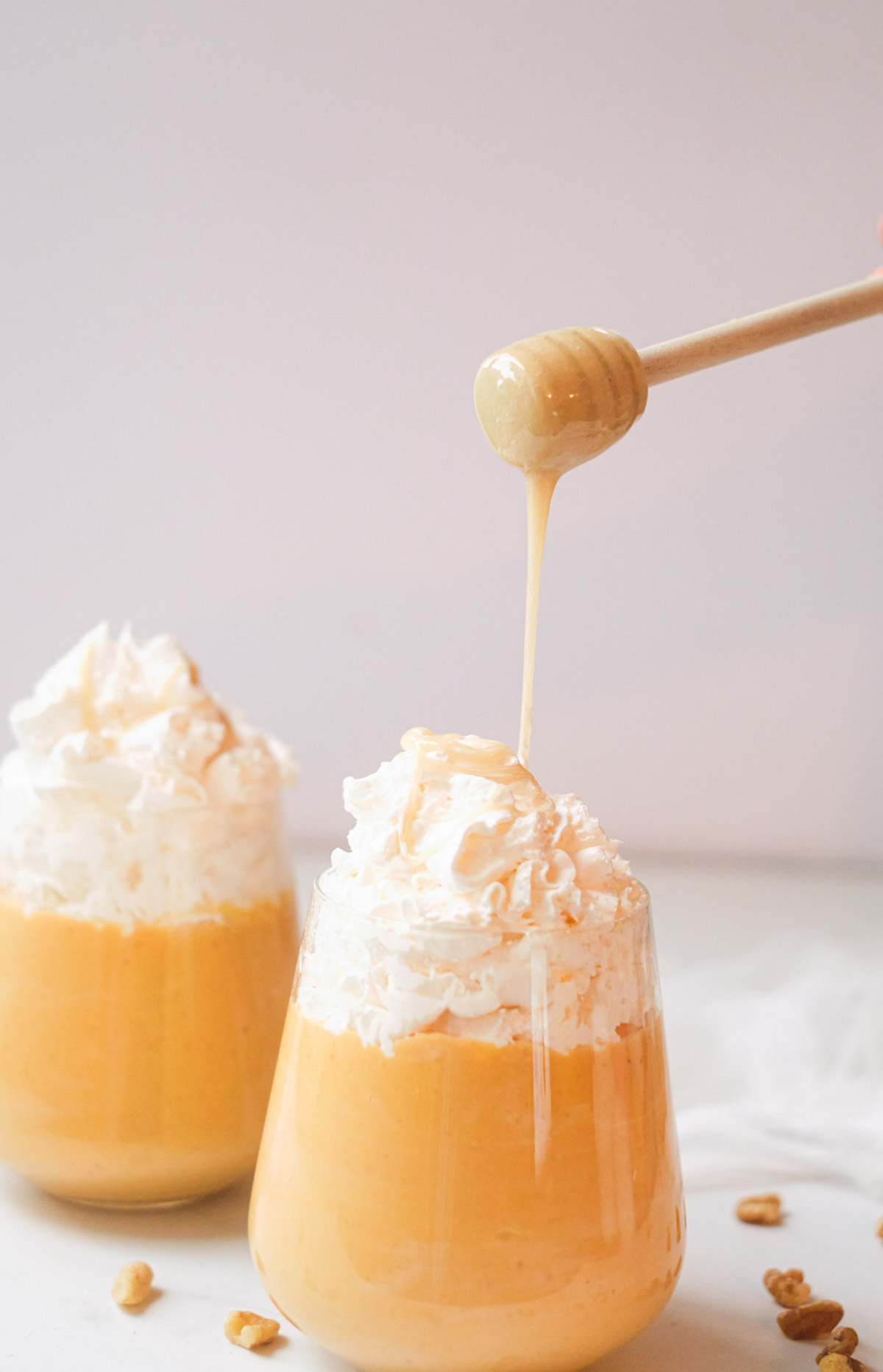 two pumpkin smoothies topped with whipped cream and a drizzle of honey
