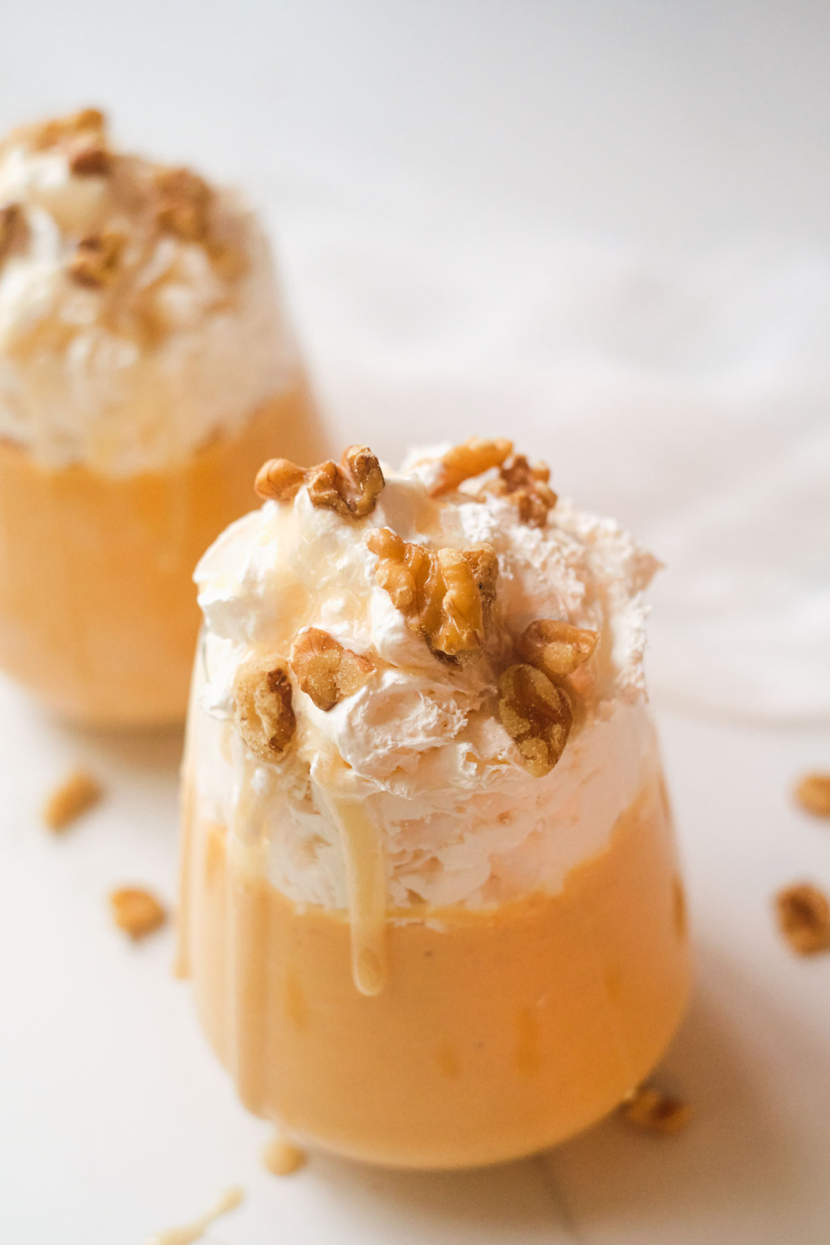 two glasses filled with pumpkin smoothie and topped with whipped cream and nuts