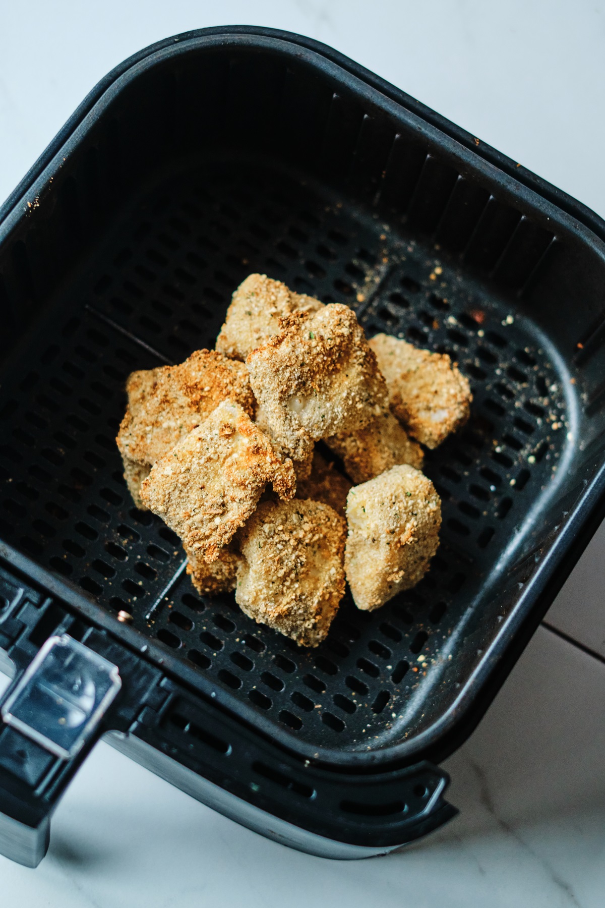 Cooked fish in air fryer basket.