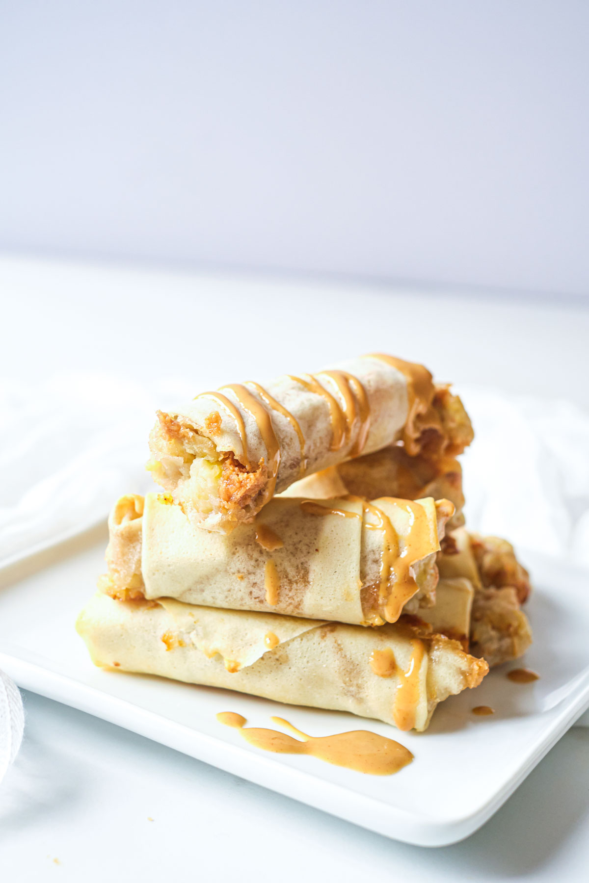 a stack of the completed air fryer peanut butter banana spring rolls on a white square plate