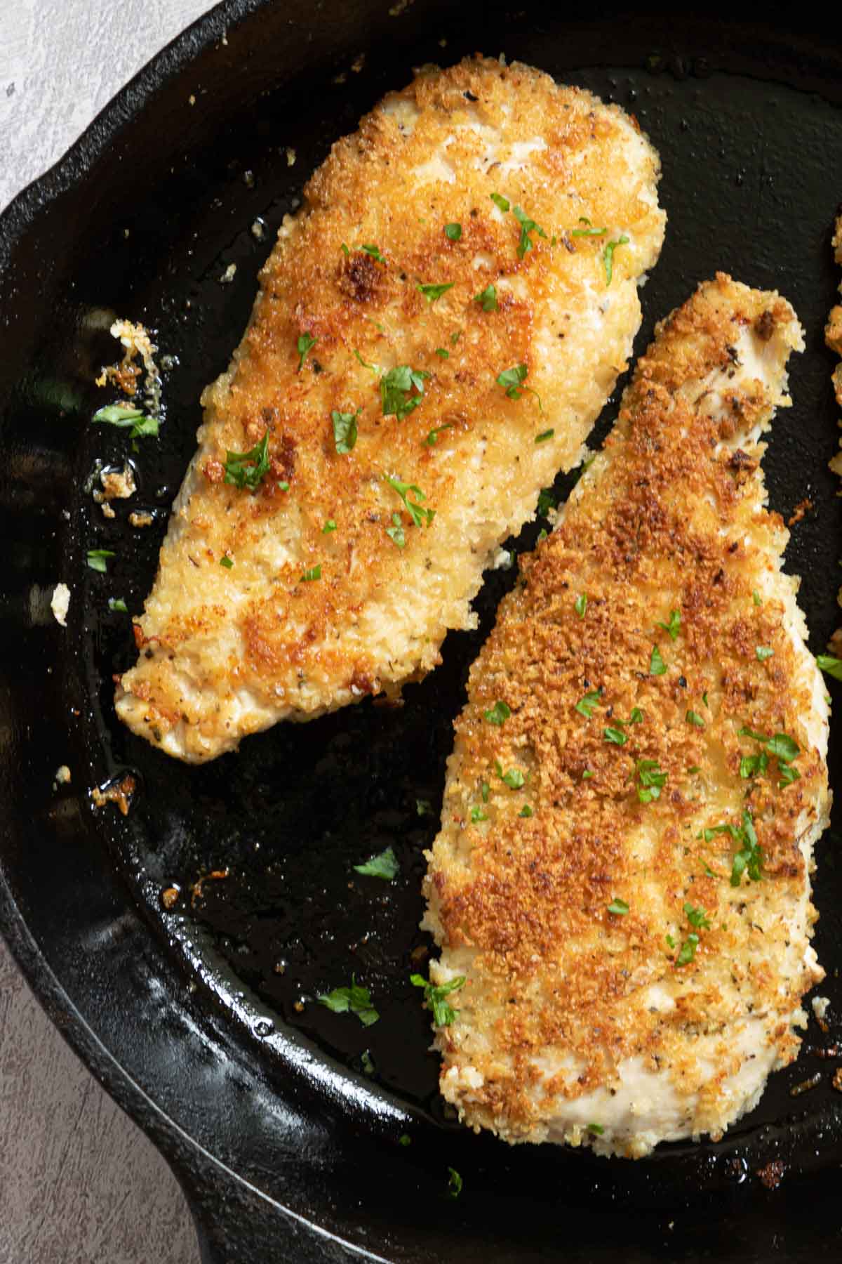 close up view of two pieces of parmesan crusted chicken in a skillet