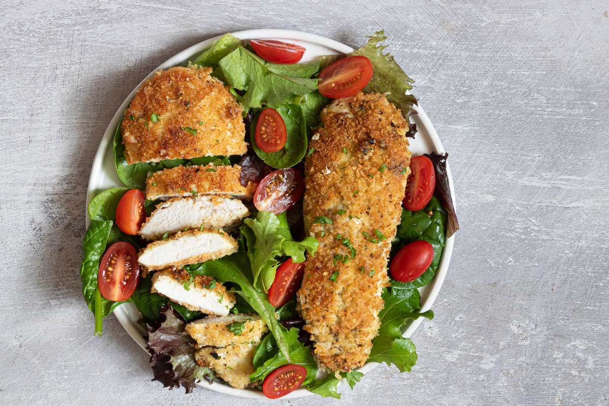 top down view of a white plate filled with parmesan crusted chicken and a salad
