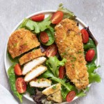 one serving of the completed parmesan crusted chicken served on top of a green salad
