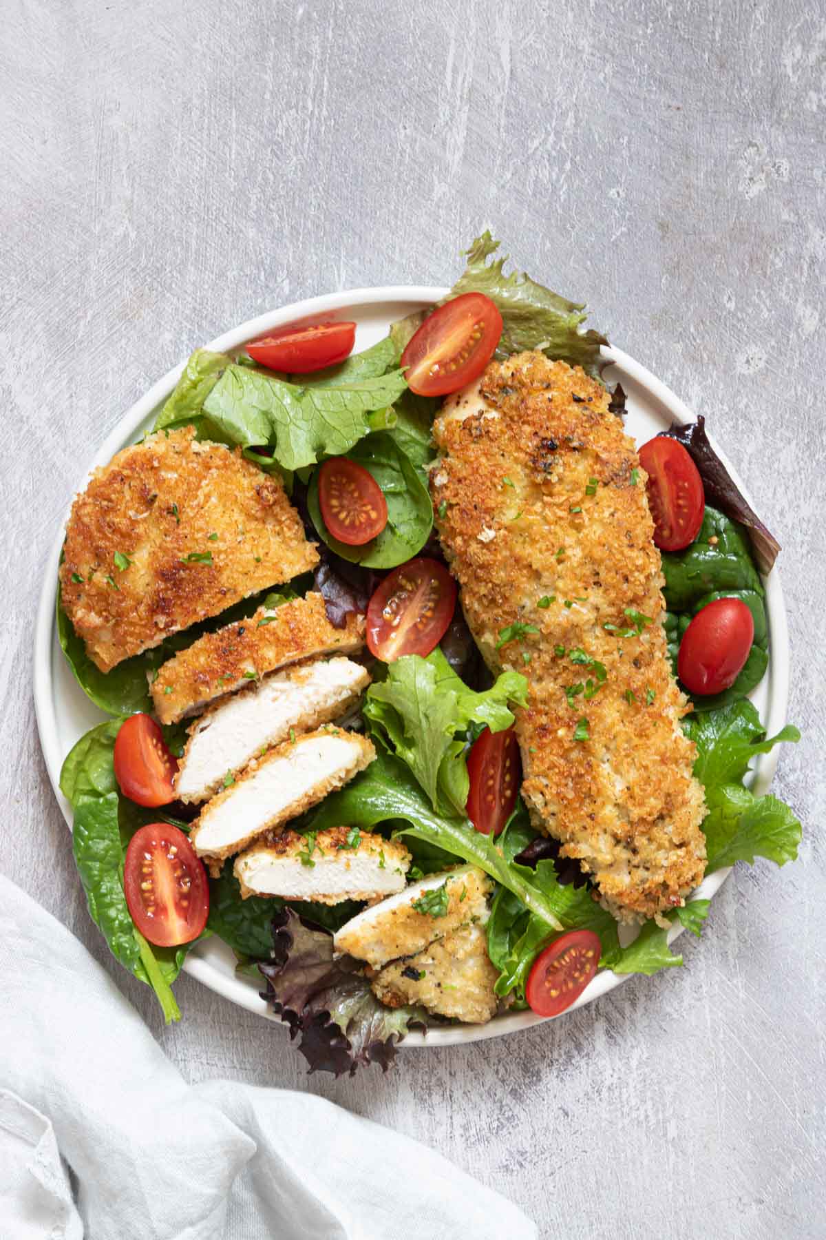 one serving of the completed parmesan crusted chicken served on top of a green salad