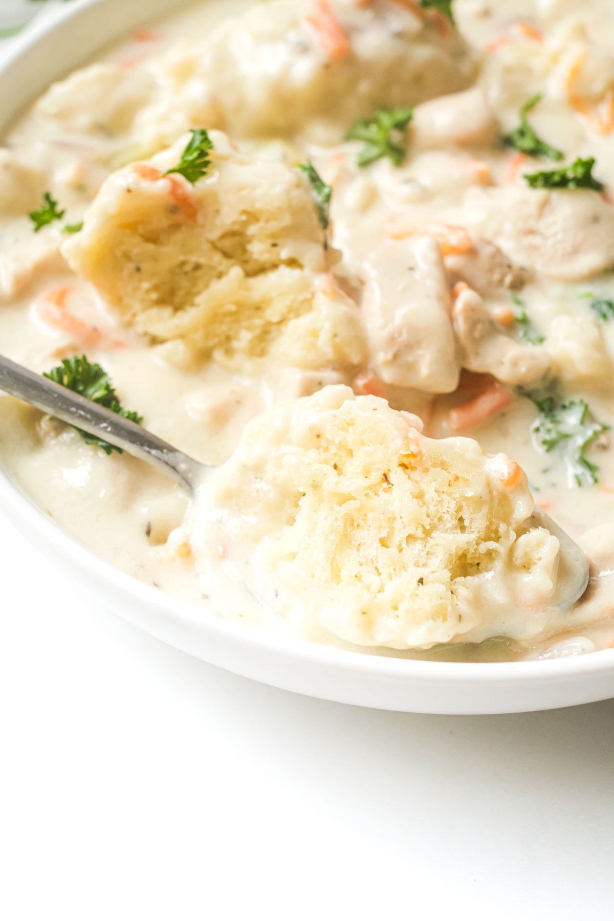 close up of a bowl of instant pot chicken and dumplings with a spoon scooping some out.