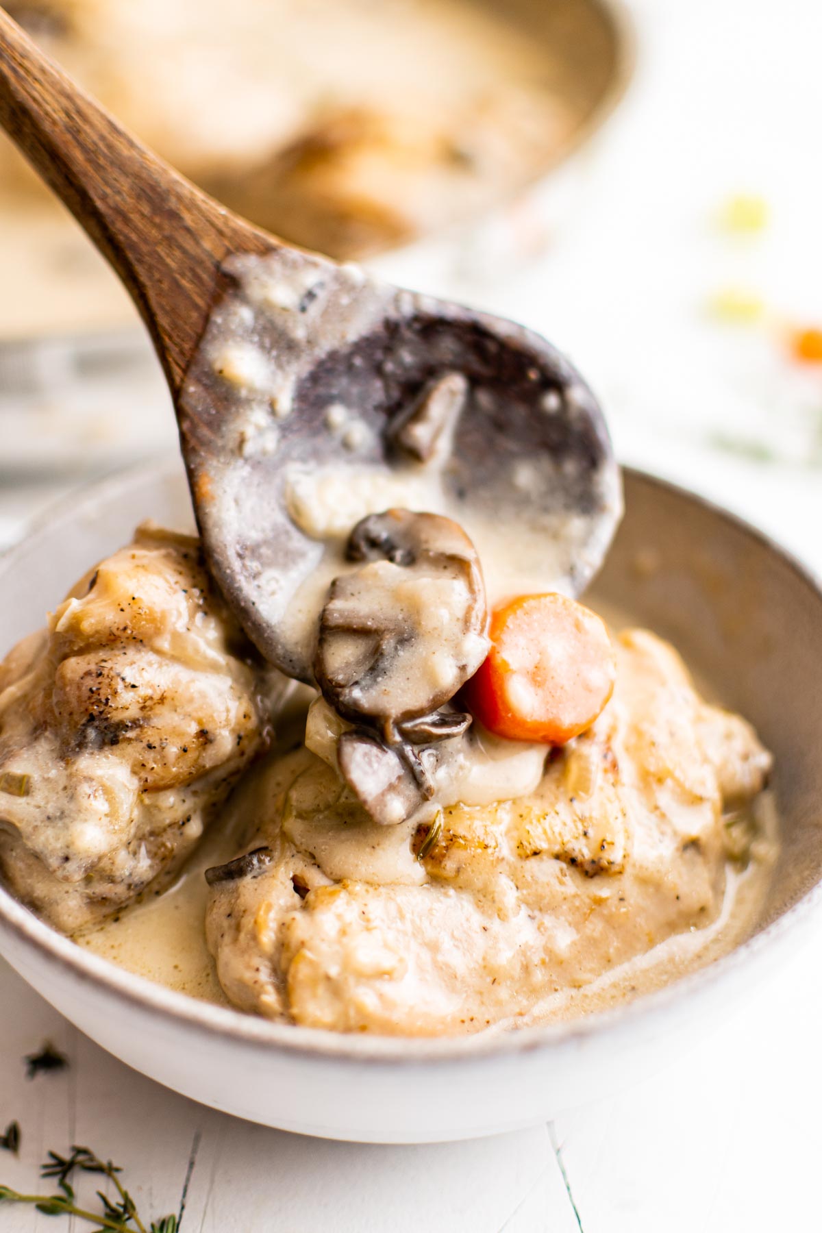 close up view of a wooden spoon scooping a portion of chicken fricassee into a bowl