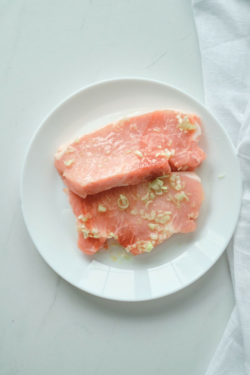 Pork being marinated on a white plate.