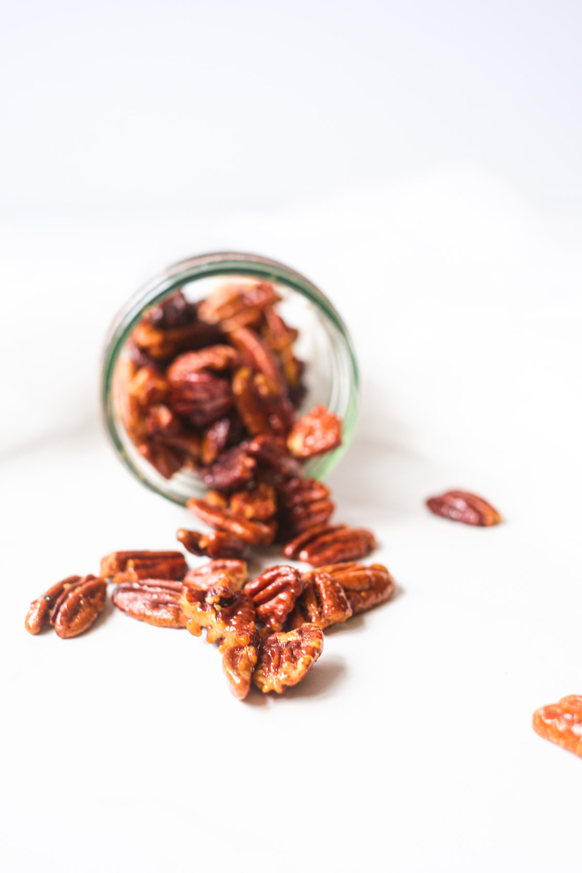 a jar of air fryer pecans on its side with pecans coming out onto the counter