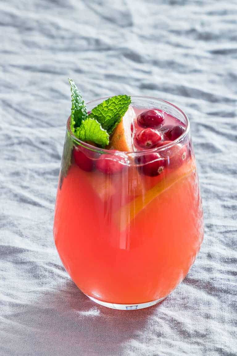 a glass of festive punch garnished with fruit and mint