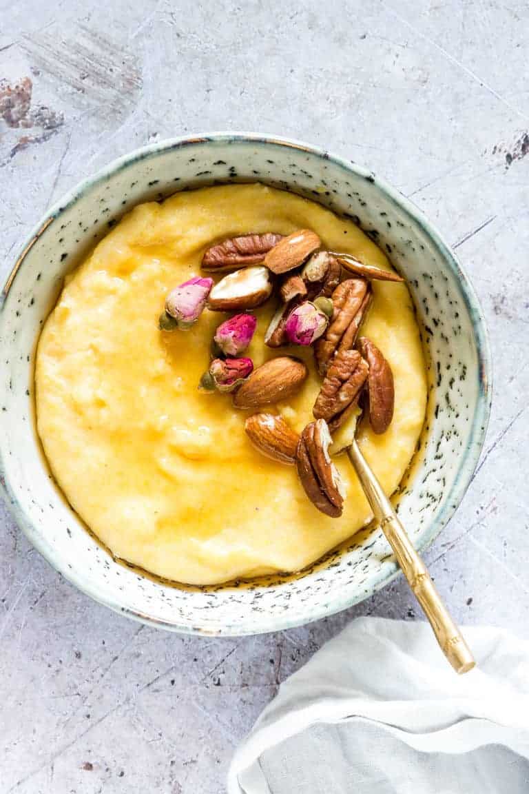 instant pot polenta breakfast porridge topped with nuts and served in a blue ceramic bowl with a gold spoon