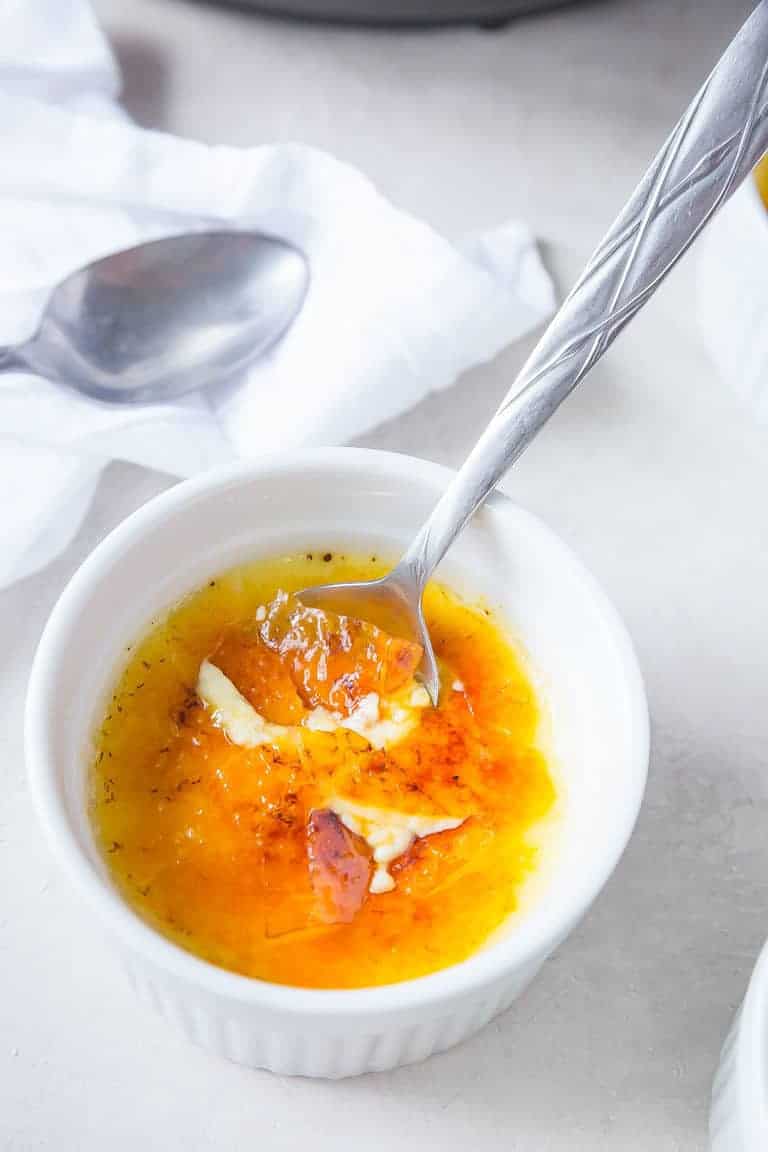 A single serving of Instant Pot Creme Brulee with a silver spoon dipped inside the ramekin
