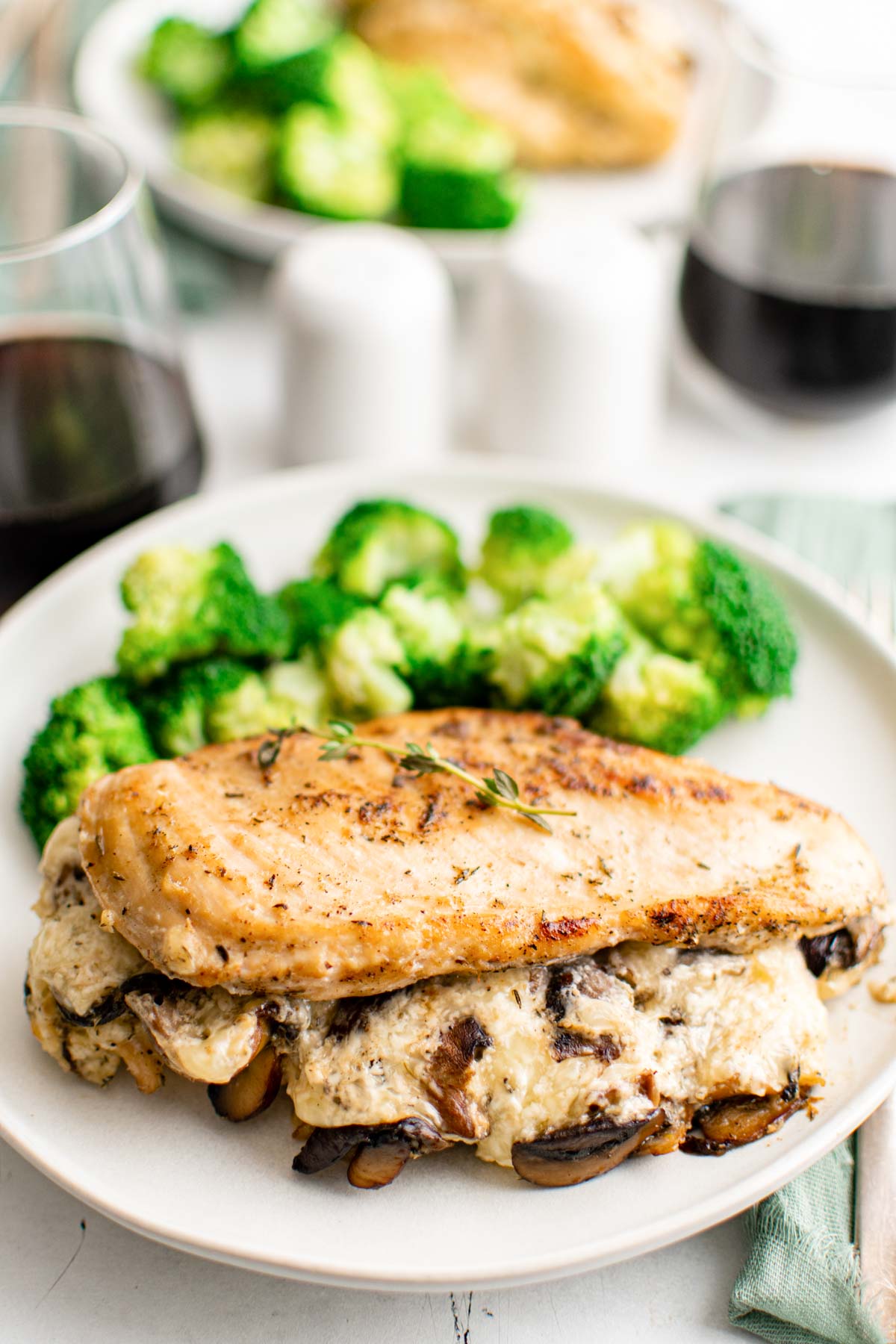 the completed mushroom stuffed chicken breast served with a side of broccoli on a white dinner plate with a glass of red wine