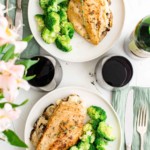 top down view of two place settings of mushroom stuffed chicken breast, broccoli and glasses of red wine