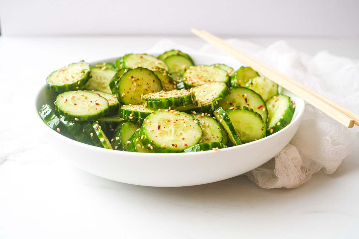 profile view of a white bowl filled with asian cucumber salad