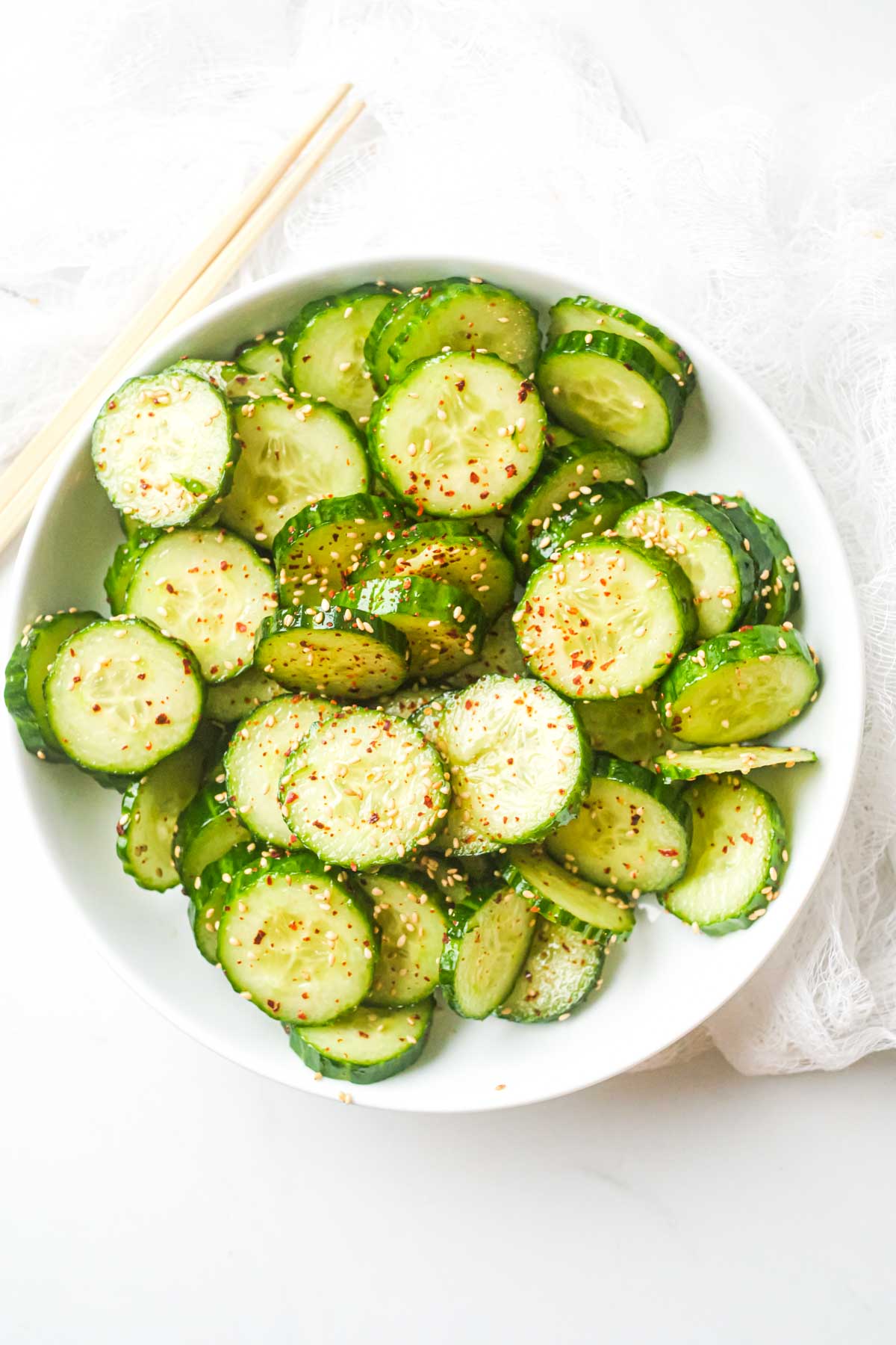 one serving of asian cucumber salad in a white bowl with a pair of chopsticks